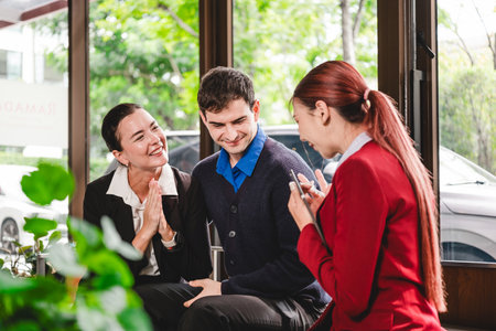 Smiling professionals in a casual meeting by a window, discussing plans and celebrating good news while viewing a smartphone.の写真素材
