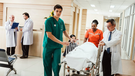 Healthcare team in a hospital corridor transports a patient on a stretcher while doctors consult nearby.の写真素材