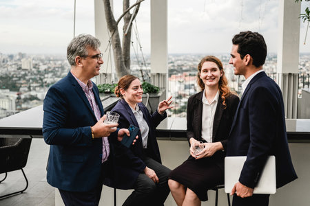 Four professionals network on a rooftop terrace, sharing drinks and conversation with a city skyline...