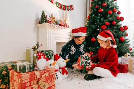 Woman and child in Santa hats open Christmas gifts beside a decorated tree in a cozy living room, surrounded by snowman decor and festive ornaments, capturing joy, togetherness, and holiday cheer.の写真素材
