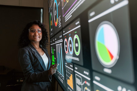 A professional Indian businesswoman interacts with a large digital dashboard displaying charts and...