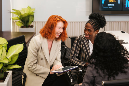 Three womenâ€”Caucasian, African, and Indianâ€”collaborate and laugh together in a modern...