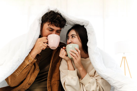 A couple cozily shares warm drinks under a soft blanket, smiling in a bright, relaxed spaceâcapturing warmth, affection, and connection perfect for lifestyle, wellness, or Valentineâs themes.の写真素材