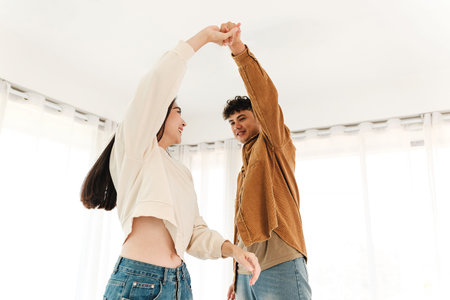 A joyful couple dances indoors, sharing a carefree moment filled with love and connection. Surrounded by soft natural light, they express harmony, energy, and the simple happiness of being together.の写真素材