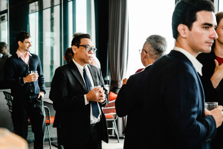 Professionals in suits network and chat at a corporate reception, holding drinks in a modern office...