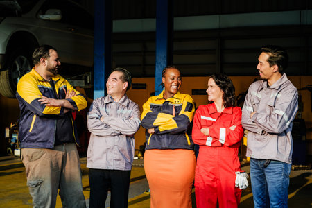 Auto repair team stands with arms crossed in a garage, smiling in work uniforms near a vehicle lift.