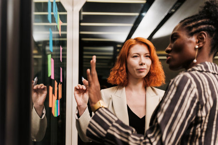 Two professionals collaborate at a glass board, organizing colorful notes and discussing strategy...