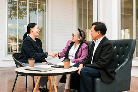Three adults meet on a porch, sharing coffee while two women shake hands, suggesting a friendly...