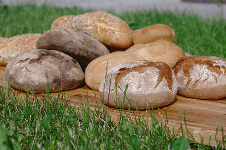 Assortiment fresh bread, baguette, buns on a wooden stand on a background of green grassの写真素材