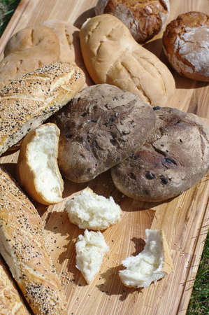 Assortiment fresh bread, baguette, buns on a wooden stand on a background of green grassの写真素材