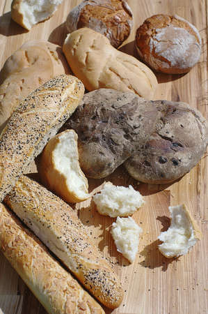 Assortiment fresh bread, baguette, buns on a wooden stand on a background of green grassの写真素材