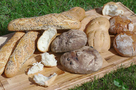 Assortiment fresh bread, baguette, buns on a wooden stand on a background of green grassの写真素材
