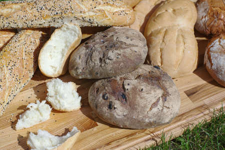 Assortiment fresh bread, baguette, buns on a wooden stand on a background of green grassの写真素材