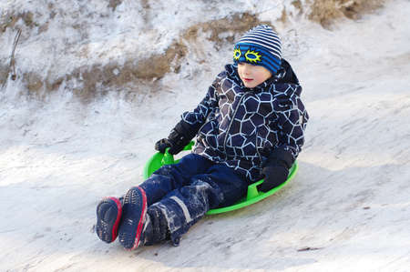 Cute Child sledding. Toddler boy riding a sledge in the snowの写真素材