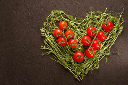 heart made of young pea shoots and cherry tomatoes on black background; Heart symbol. Vegetables diet conceptの写真素材