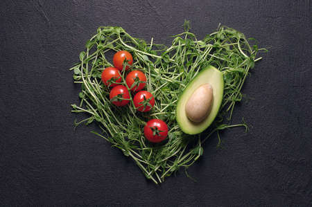 heart made of young pea shoots and cherry tomatoes on black background; Heart symbol. Vegetables...