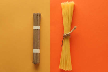 buckwheat noodle spaghetti and wholegrain spaghetti on a bright yellow and orange background. Top view. Place the textの写真素材