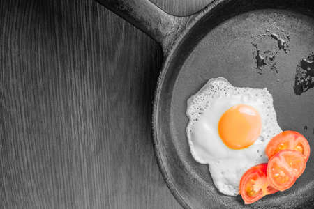 Egg, sunny side up, with fresh tomatoes in a black panの写真素材