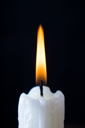 White candle burning with yellow fire on a black backgroundの写真素材