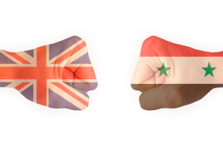 Two fists with the flag of Syria and the United Kingdom collided with each other, ready for battle isolateの写真素材