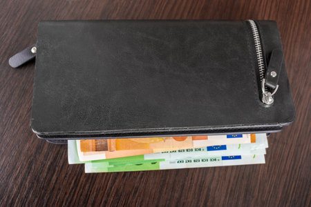 Open purse with euro cash denominations of denomination 10 20 50 100 on a wooden background. Men's wallet with cash euro.の写真素材