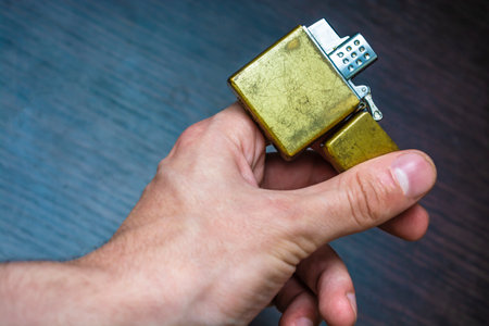 hand-held golden folding lighter on a dark background in yellow-blue tones warmth of cold