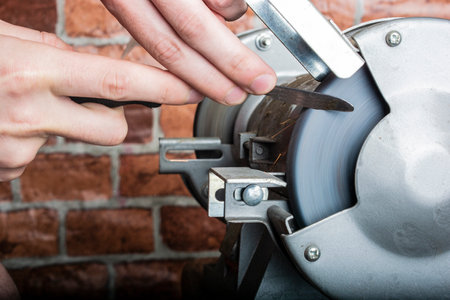 A knife sharpener and hand with a blade on a wooden table, close-up against a brick wall background