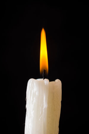 White candle burning with yellow fire on a black backgroundの写真素材