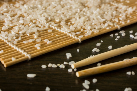 sushi mat on which scattered rice next to lies chopsticks all on the background of a wooden tableの写真素材