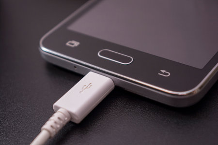 black smartphone on a black matte background with a white connected cableの写真素材
