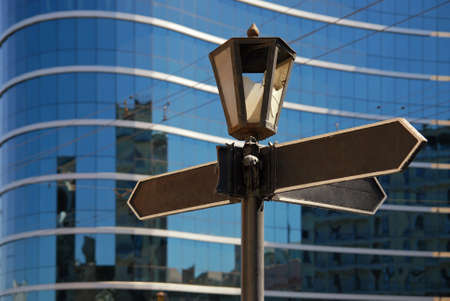 Blank signpost with ancient lamp against business buildingの写真素材
