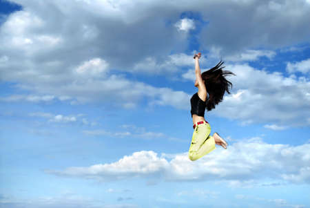 A young girl jumping in front of blue sky and cloudsの写真素材