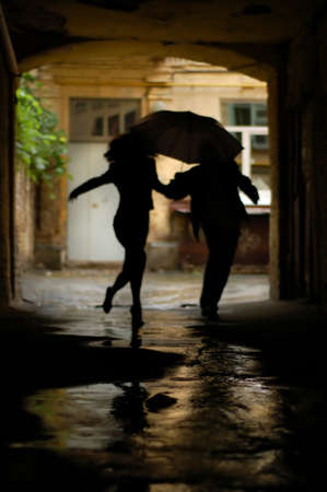 silhouette of couple with umbrella running from rainの写真素材