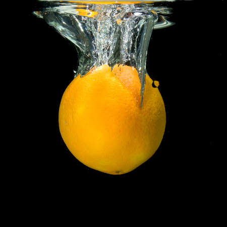 orange dropped into water on blackの写真素材