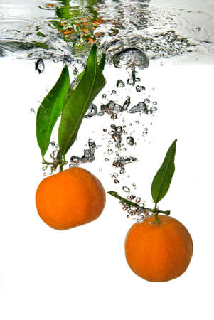tangerine dropped into water with bubbles on whiteの写真素材