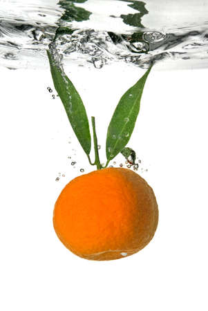 tangerine dropped into water with bubbles on whiteの写真素材