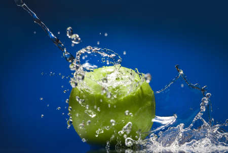 Green apple with water splash on blue backgroundの写真素材