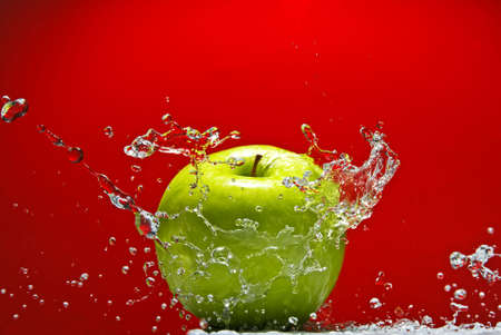 Green apple with water splash on red backgroundの写真素材