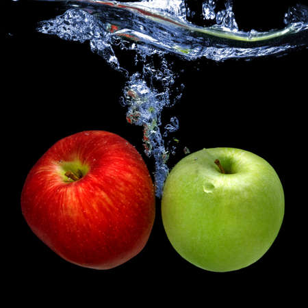 apples dropped into water with splash isolated on blackの写真素材