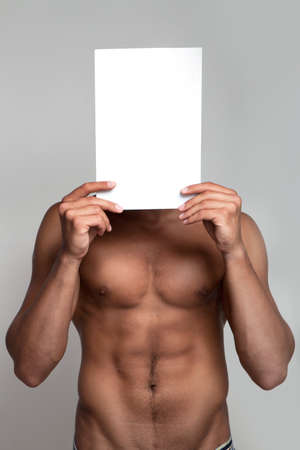 Muscular naked man holding white empty paperの写真素材