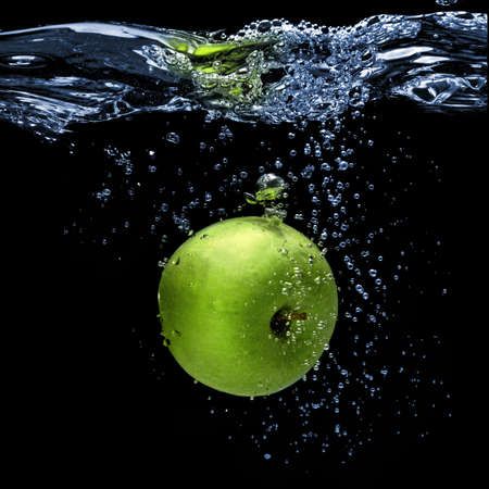 green apple dropped into water with splash isolated on blackの写真素材