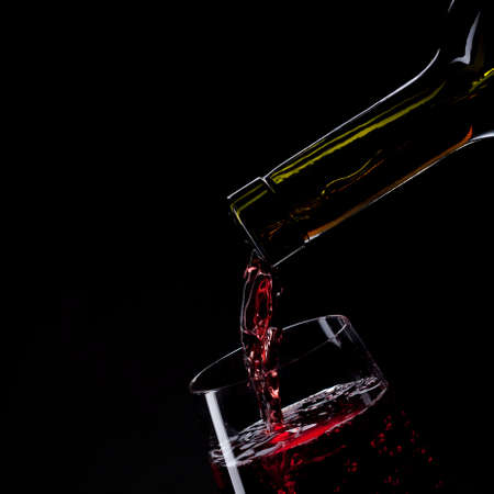 red wine pouring into wine glass isolated on black