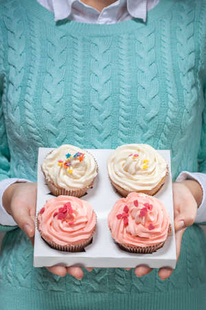 young woman holding a box of colorful cupcakes decorated with hearts and stars, isolated on whiteの写真素材