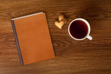 woman with cup of tea, cookies and book on wooden tableの写真素材