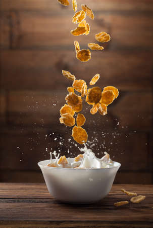 Falling corn flakes with milk splash on wooden backgroundの写真素材