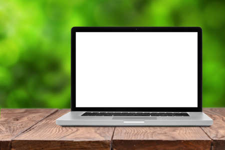Laptop with blank screen on wooden empty brown table on green natural summer blurred backgroundの写真素材