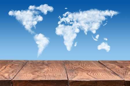 empty wooden table with world map made of white puffy clouds on sky as backgroundの写真素材