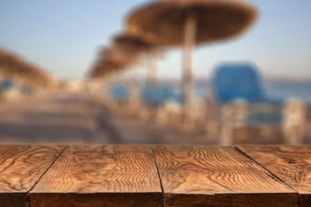 Empty wooden table with blurred beach with straw umbrellas on sunrise on backgroundの写真素材