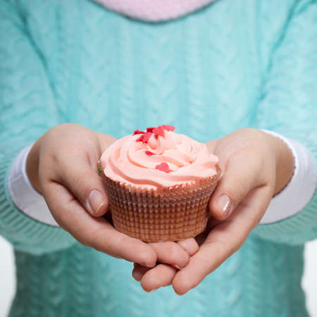 Young woman holding a pink cupcake decorated with hearts, isolated on white backgroundの写真素材