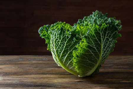 Single head of Savoy cabbage on rustic wood against black backgroundの写真素材